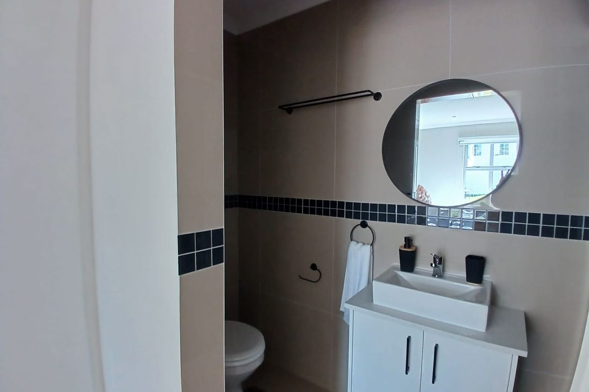 A modern bathroom featuring a white vanity cabinet with a vessel sink, neutral wall tiles with a decorative border, and a circular mirror.