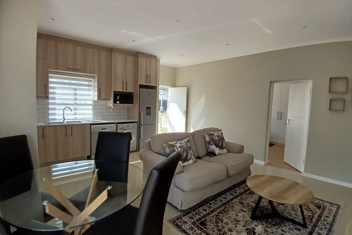 Open-plan living area featuring a modern kitchen with light wood cabinetry, subway tile backsplash, and integrated appliances, flowing into a comfortable lounge space.