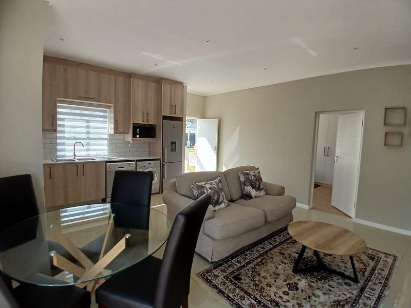 Open-plan living area featuring a modern kitchen with light wood cabinetry, subway tile backsplash, and integrated appliances, flowing into a comfortable lounge space.