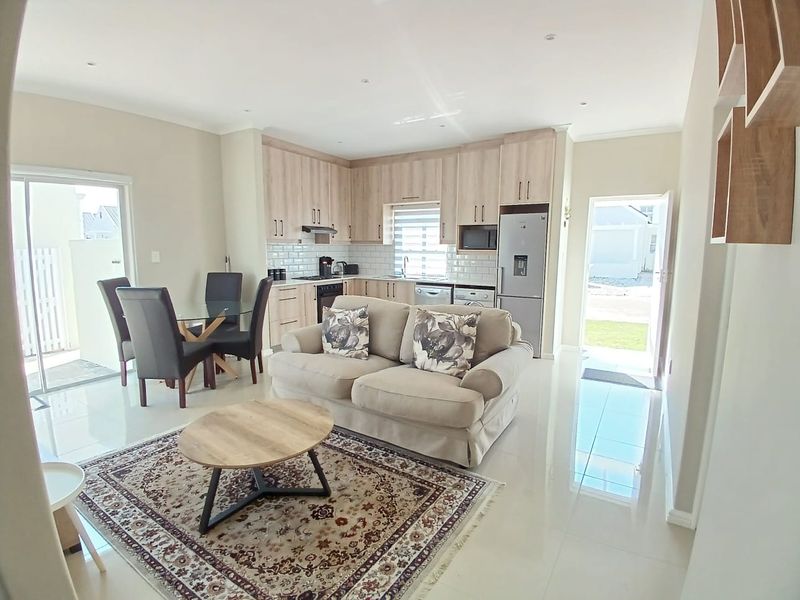 Modern open-plan living area featuring a well-appointed kitchen with light wood cabinetry, subway tile backsplash, and direct access to the outdoor patio.