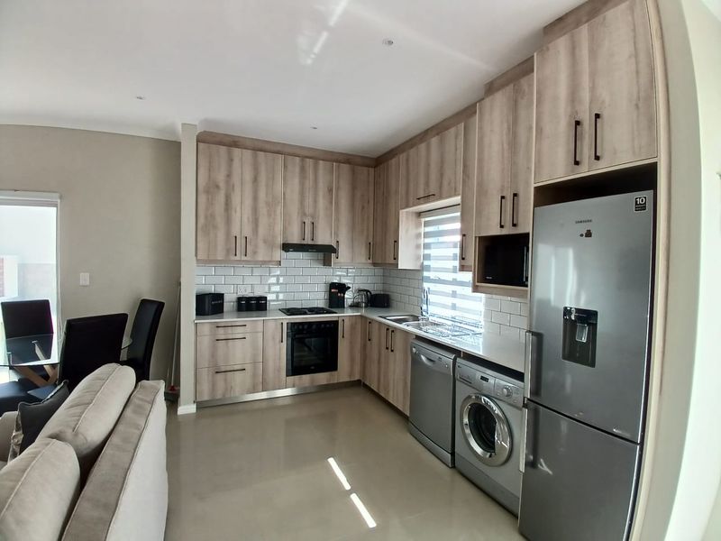 Modern open-plan kitchen featuring light wood-grain cabinetry, subway tile backsplash, integrated appliances, and sleek tiled flooring, seamlessly connecting to the living and dining area.