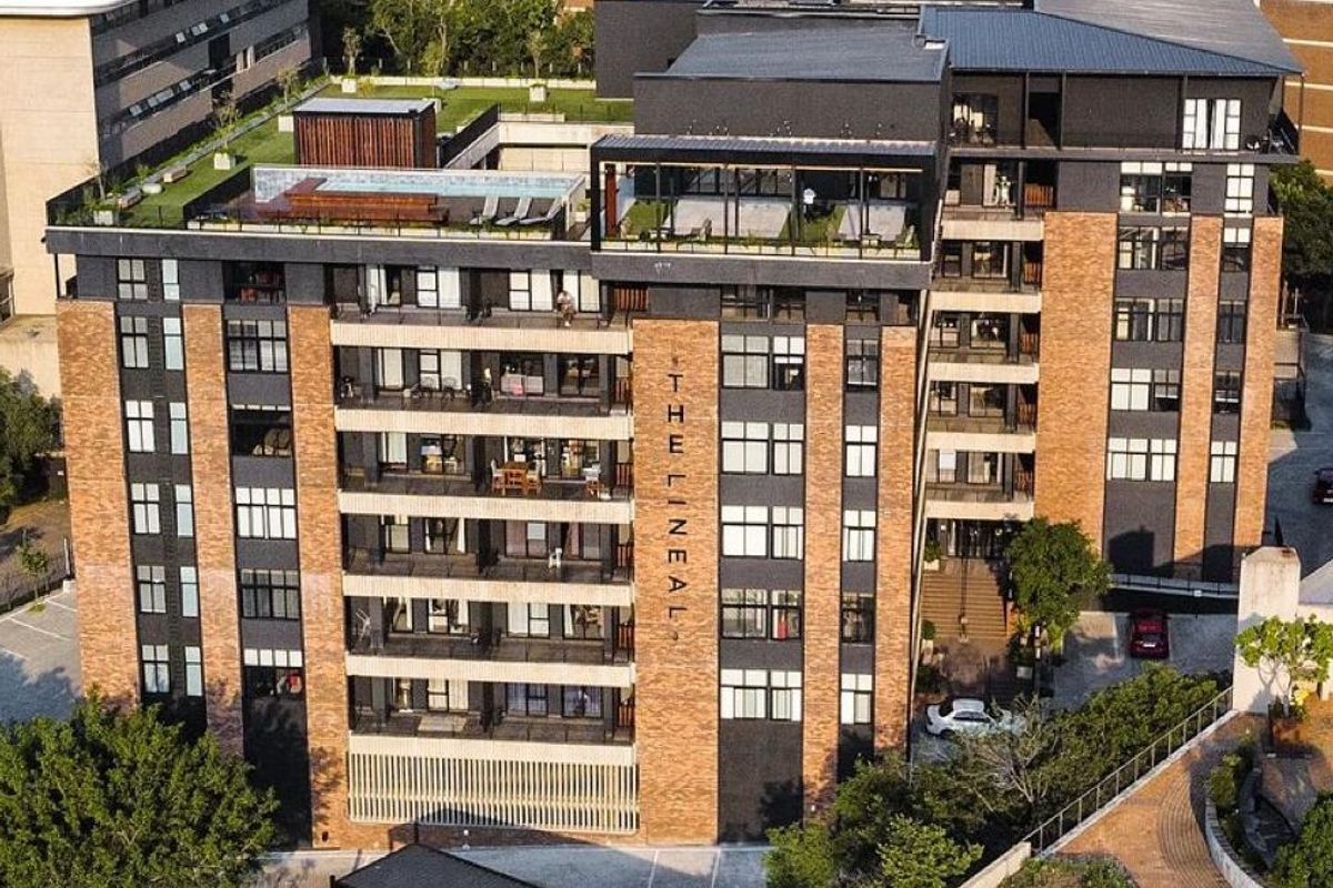 Aerial view of The Lineal apartment complex, showcasing its modern brick and dark metal facade, rooftop amenities, and secure gated entrance.