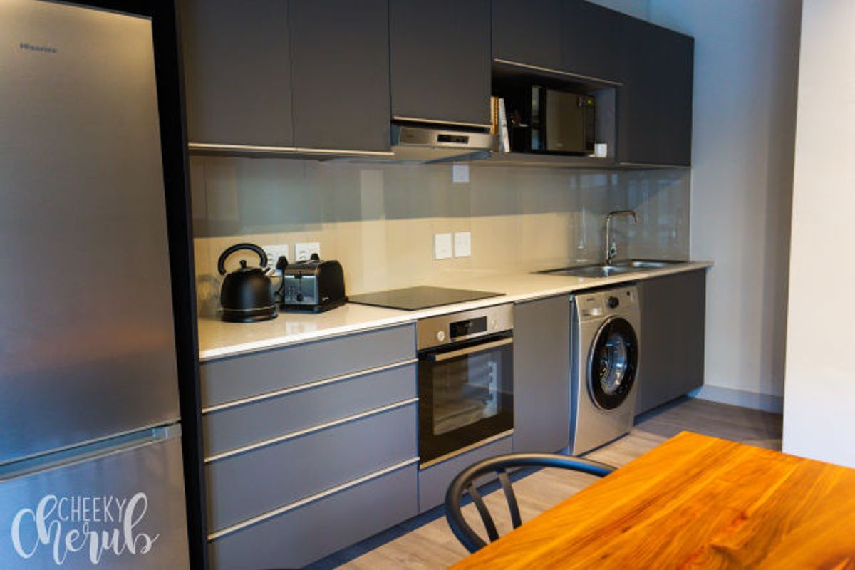 Modern kitchen featuring sleek grey cabinetry, integrated oven, electric cooktop, stainless steel sink, and built-in laundry appliance.