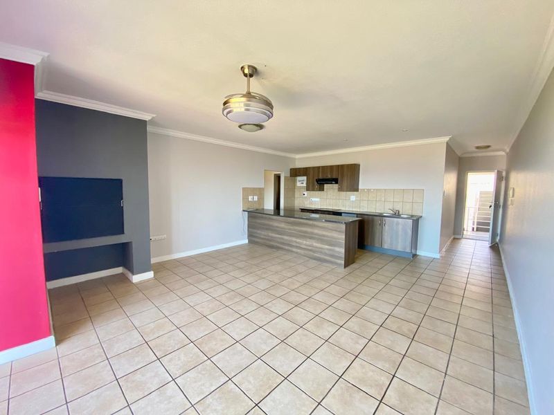Spacious open-plan living and kitchen area featuring tiled flooring, a built-in fireplace, and a functional kitchen with breakfast counter and built-in cabinetry.