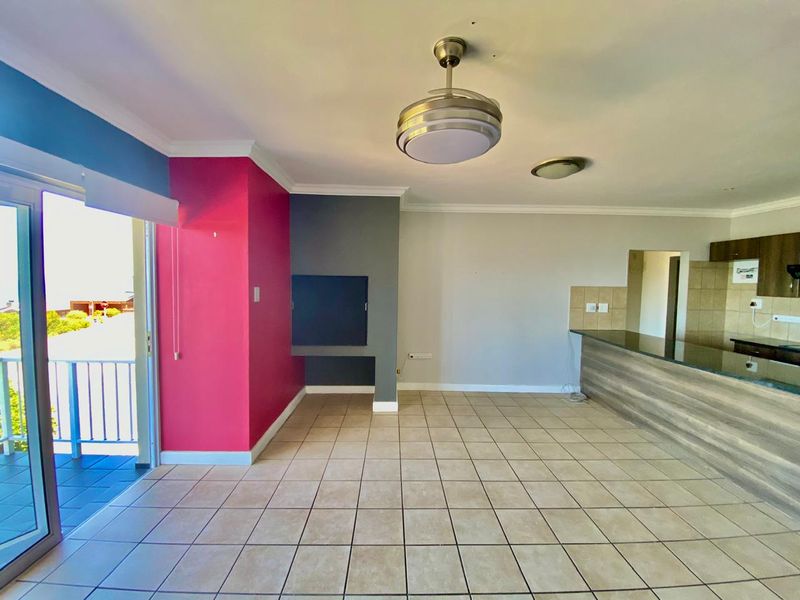Open plan living area featuring a built-in braai, breakfast bar, tiled flooring, and direct access to a balcony through sliding doors.