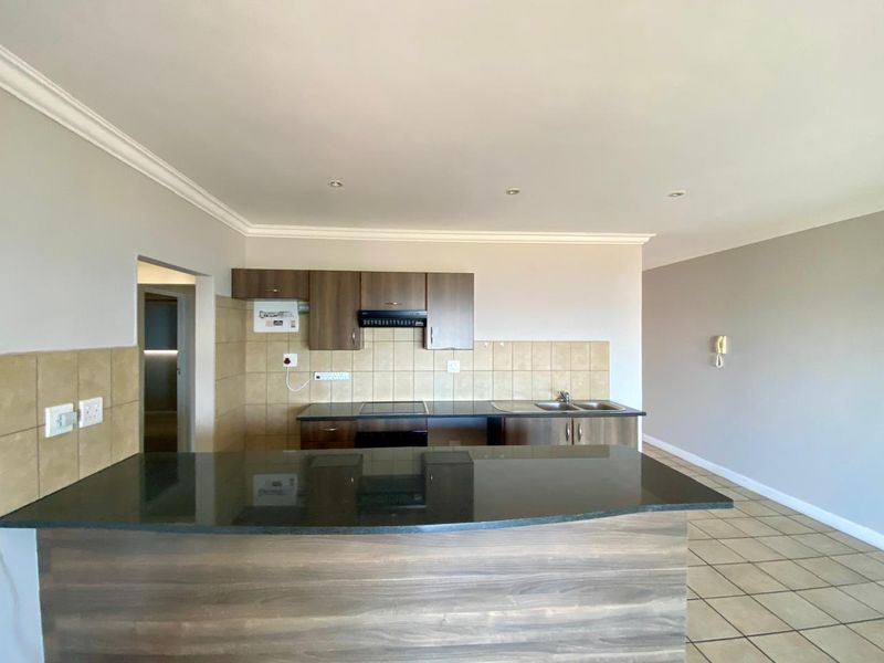 A clean, functional kitchen featuring dark wood cabinetry, granite countertops, a breakfast bar, and neutral tiled flooring with a matching backsplash.