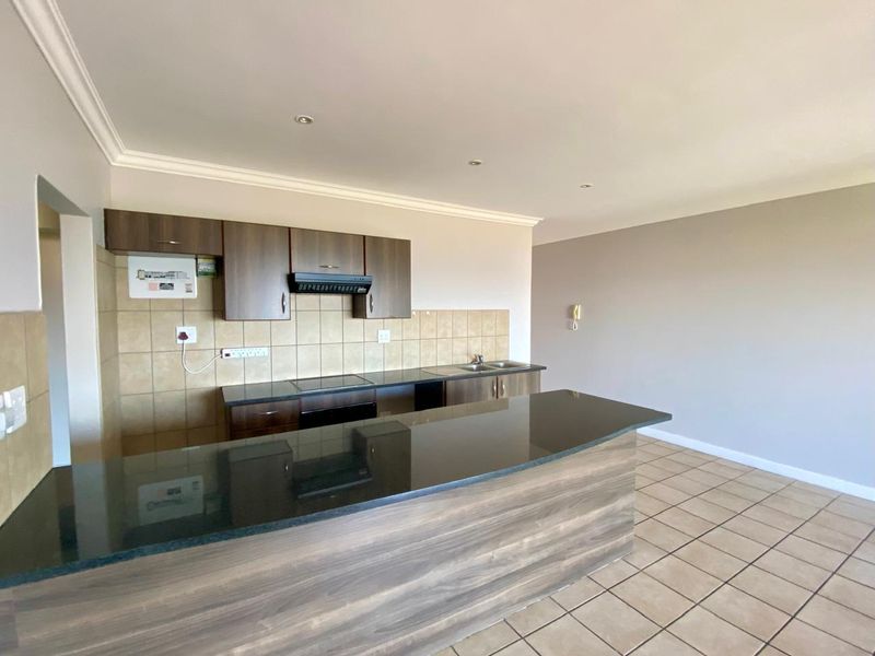Open-plan kitchen featuring dark wood cabinetry, granite countertops, integrated hob, and tiled flooring in a well-maintained, vacant apartment space.