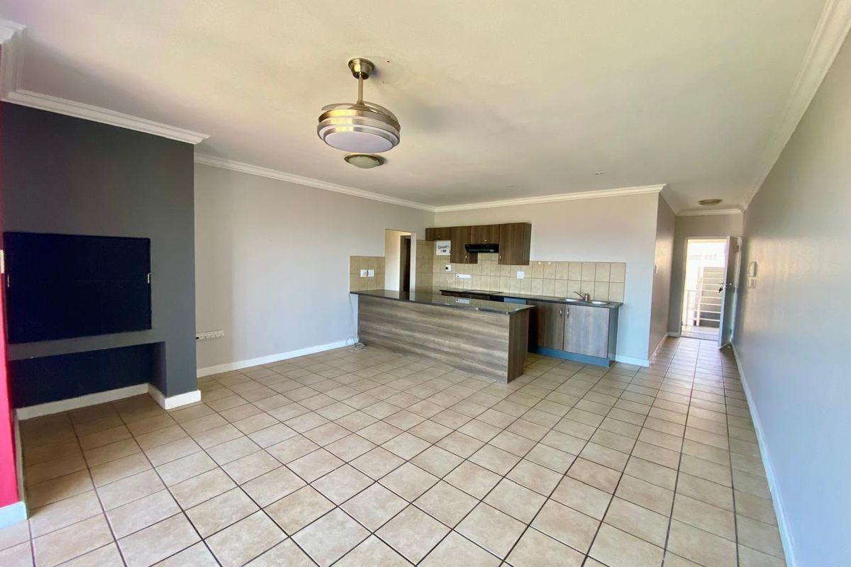 Spacious open-plan living area featuring a kitchen with built-in cabinetry, a central island, and a built-in fireplace, finished with neutral tiled flooring.
