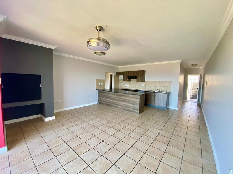 Spacious open-plan living area featuring a kitchen with built-in cabinetry, a central island, and a built-in fireplace, finished with neutral tiled flooring.
