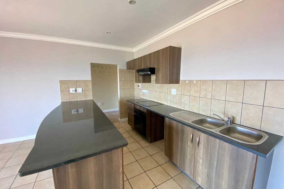 A functional kitchen featuring wood-finish cabinetry, granite countertops, a breakfast bar, and built-in appliances, including an oven and extractor fan.