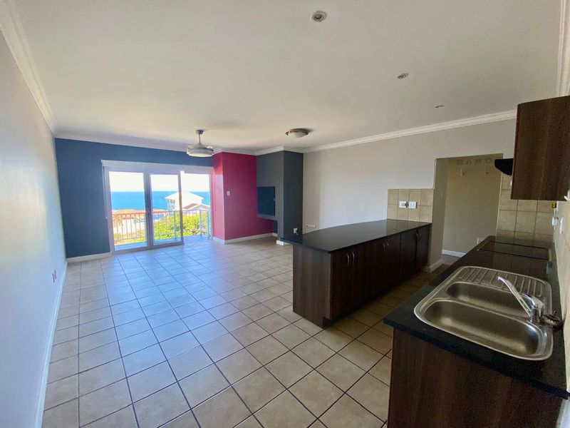Spacious open-plan living and kitchen area featuring tiled floors, a central island, and sliding doors leading to a balcony with ocean views.
