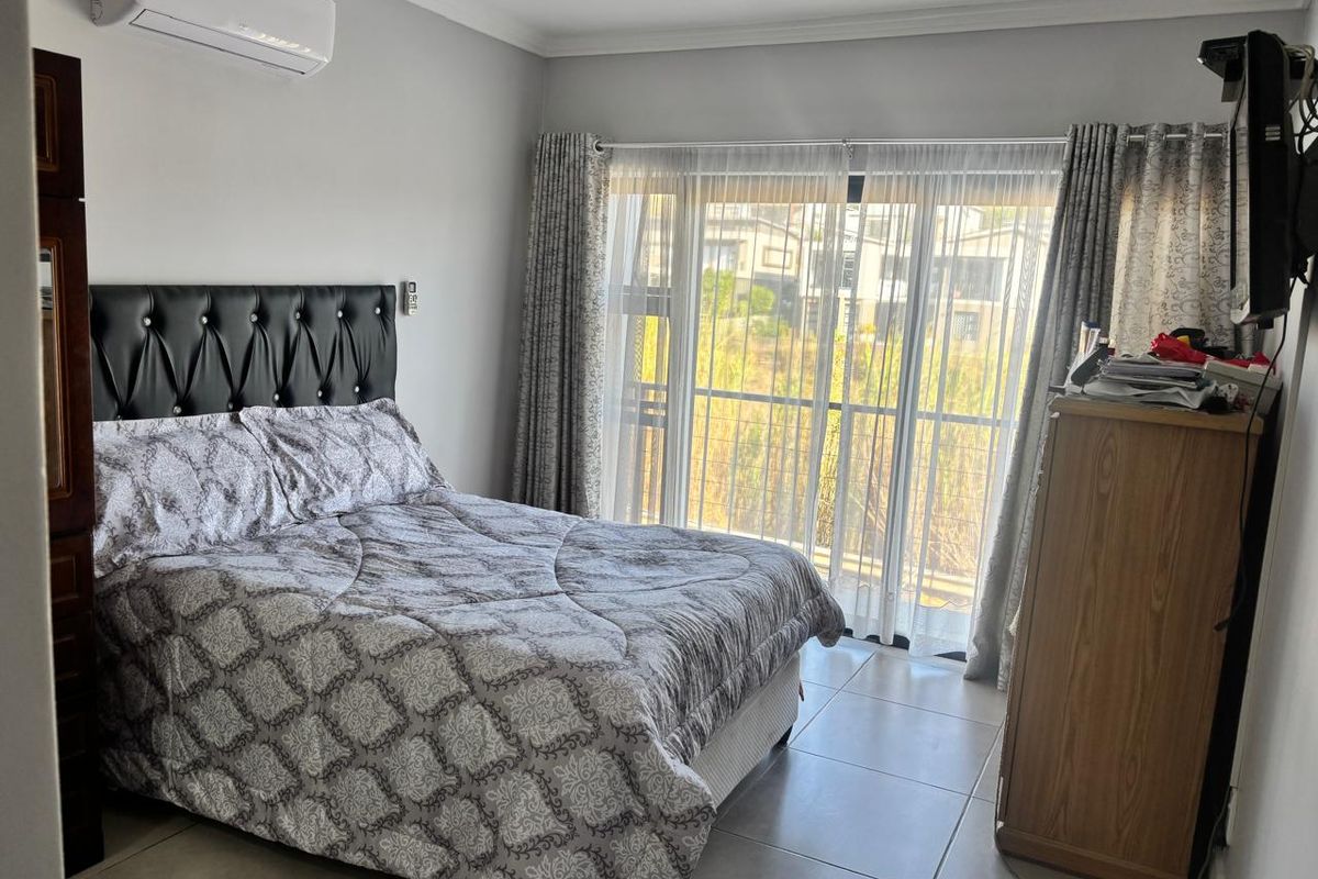 A well-maintained bedroom featuring tiled flooring, a wall-mounted air conditioning unit, and large sliding glass doors providing natural light and access to the exterior.