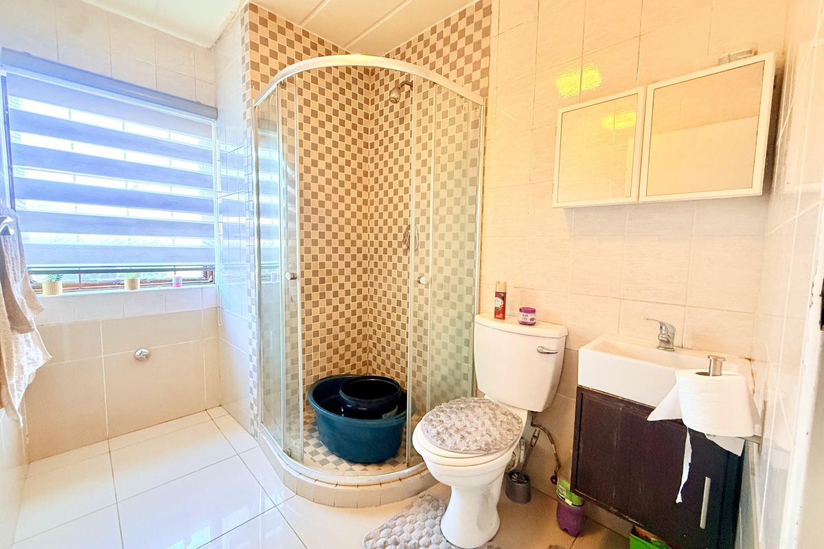 A functional bathroom featuring a corner shower enclosure, a wall-mounted vanity with basin, and a standard toilet, finished with neutral wall and floor tiles.
