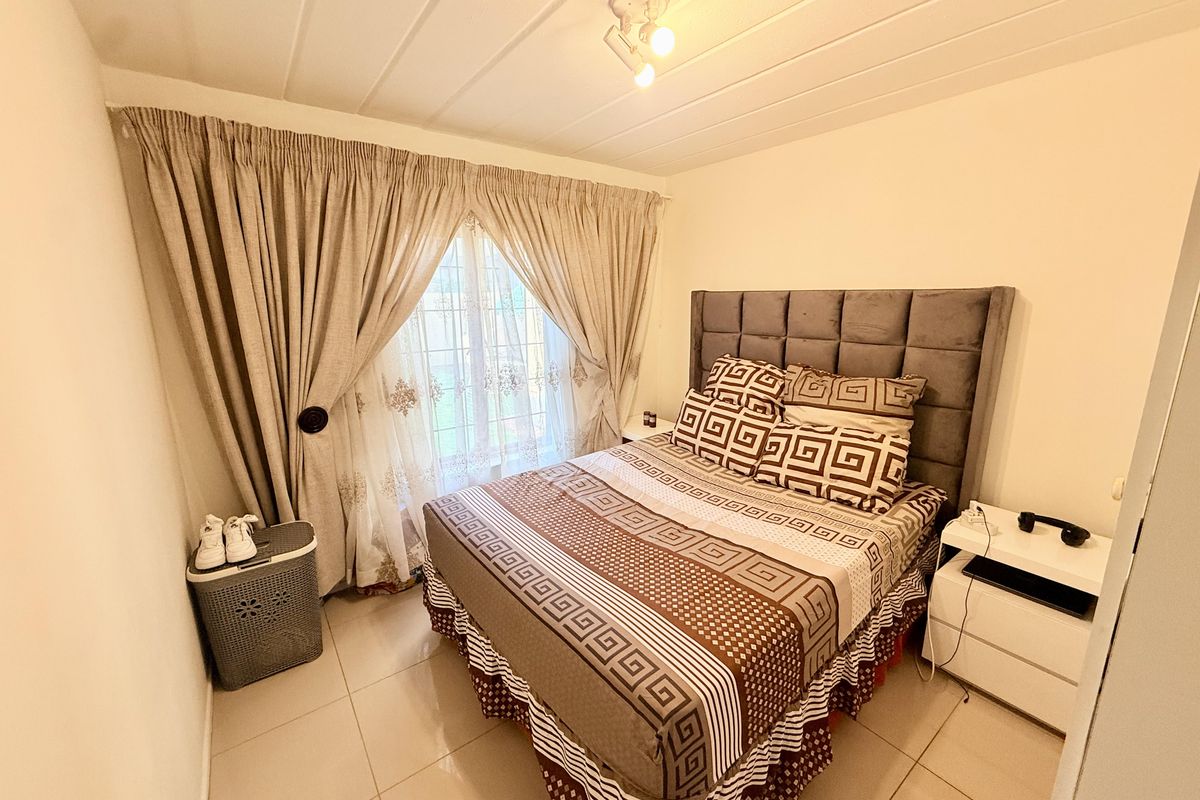 A bedroom featuring tiled flooring, a window with curtain treatments, and a ceiling-mounted light fixture.
