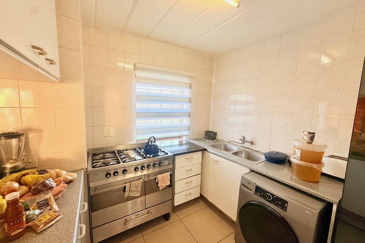 Functional kitchen featuring tiled walls, built-in cabinetry, a stainless steel gas stove, double sink, and space for a front-loading washing machine.