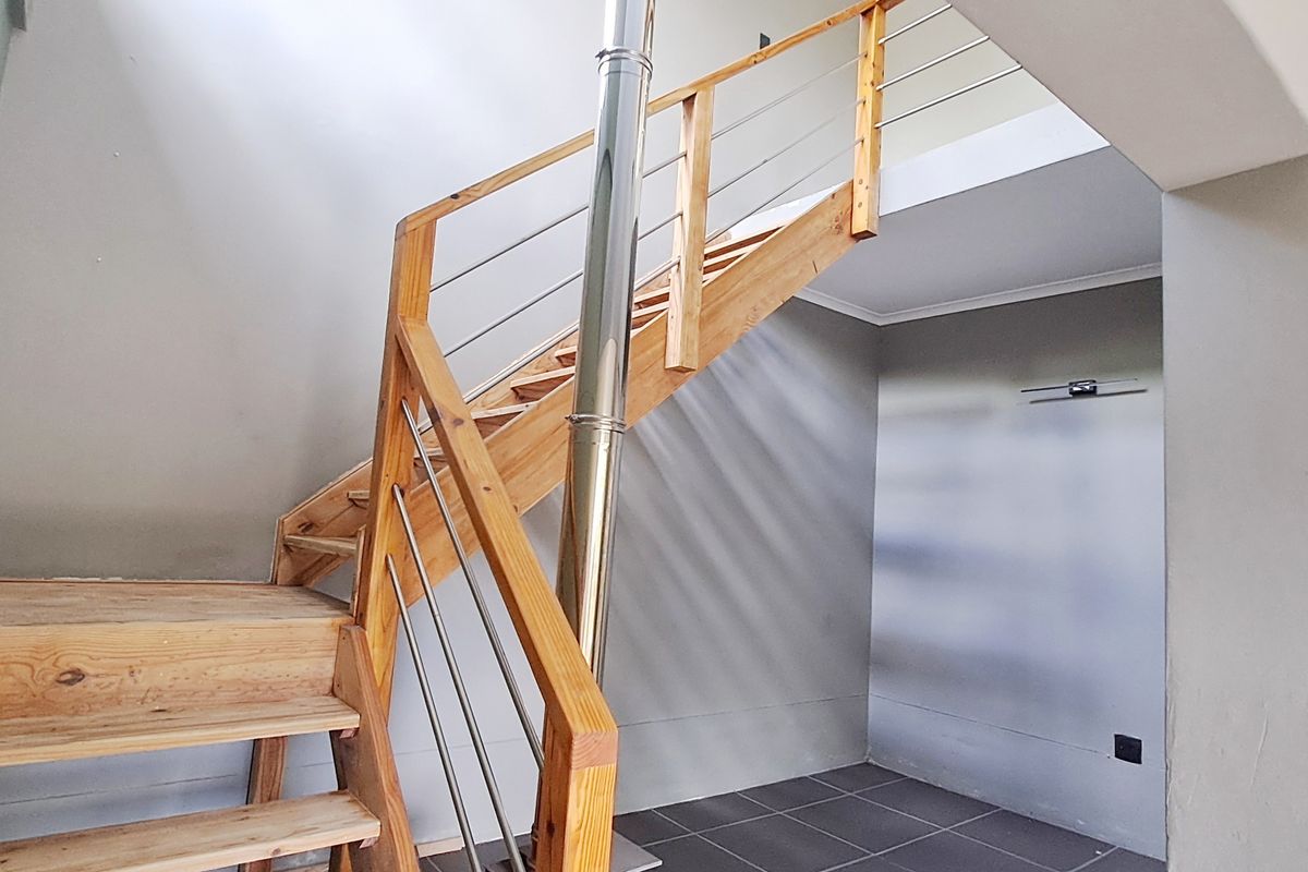 An open-plan living area featuring a wooden staircase with stainless steel balustrades, a central flue pipe, and modern tiled flooring.