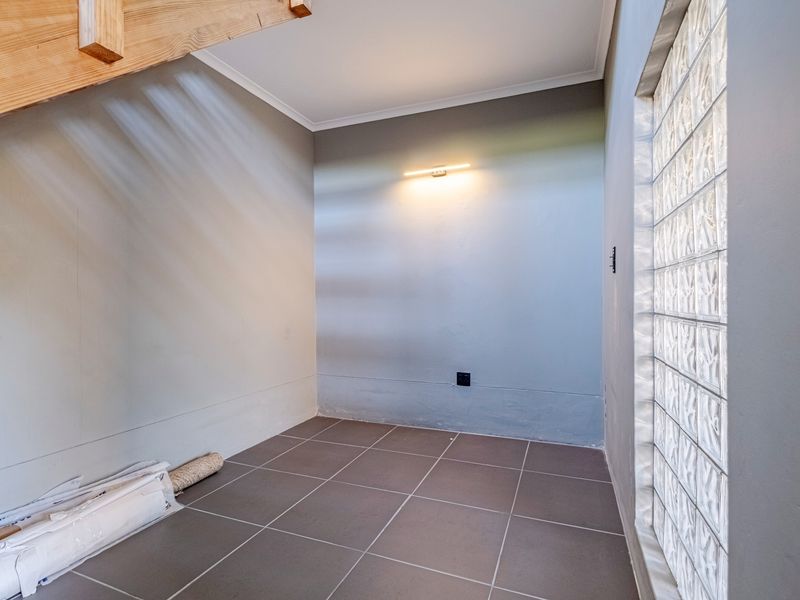 A bright, empty hallway featuring modern tiled flooring, a unique glass block wall, and an exposed wooden staircase.
