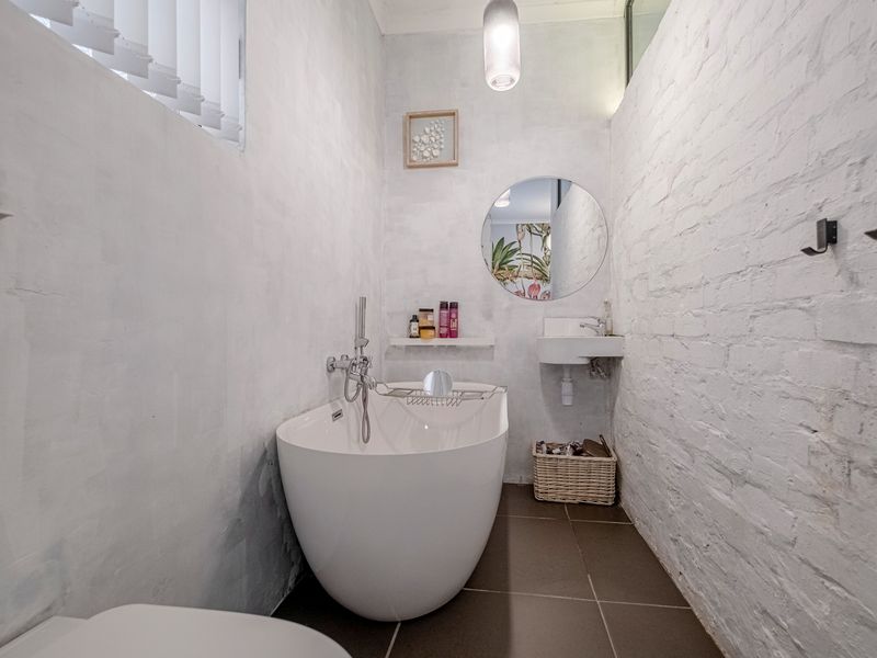A modern bathroom featuring a sleek freestanding bathtub, wall-mounted basin, and characterful painted exposed brick walls with tiled flooring.