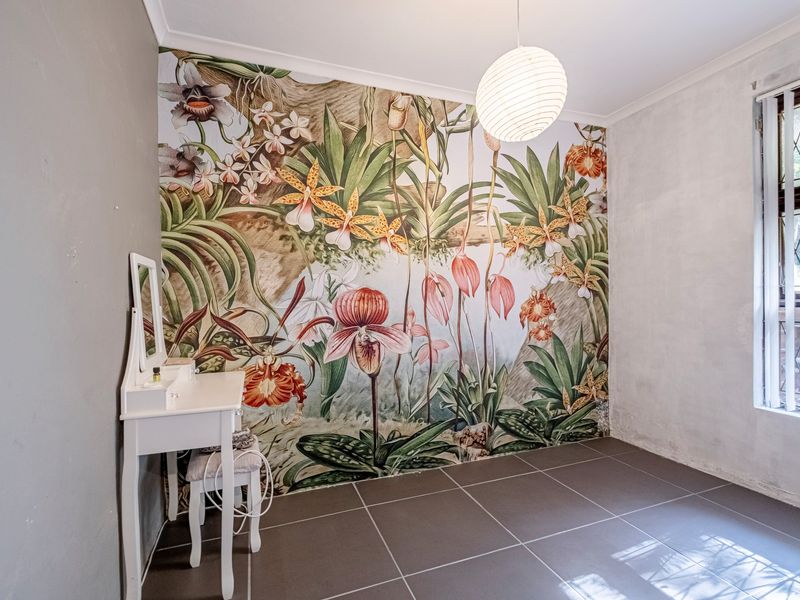 Bedroom featuring large-format floor tiles, a vibrant botanical feature wall, and a window fitted with security bars.