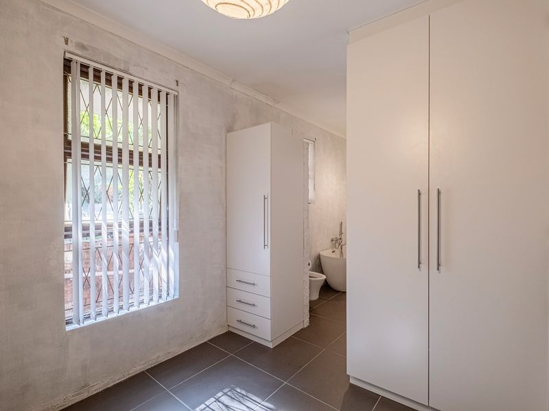 A bedroom featuring tiled flooring, built-in cupboards, and vertical blinds, with an adjacent view into a bathroom area.
