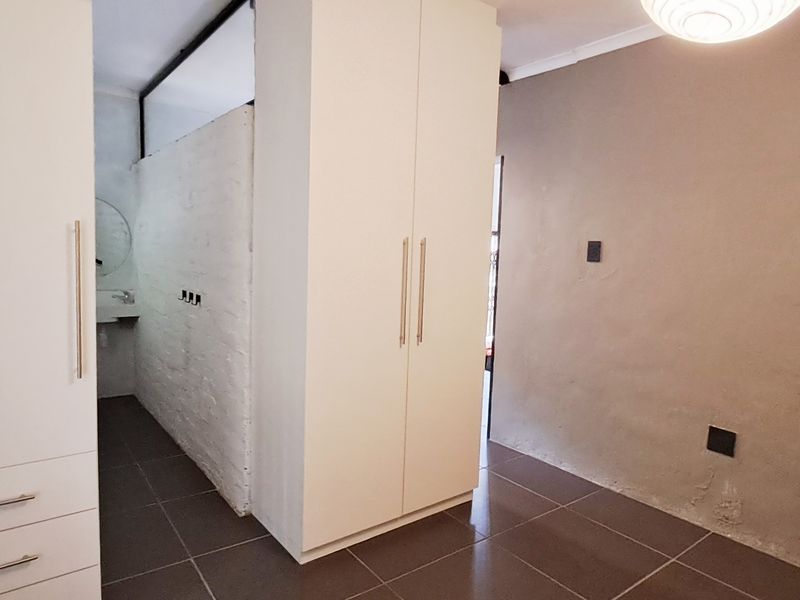A bedroom featuring built-in cupboards, tiled flooring, and an exposed brick wall, showing signs of moisture damage on the lower wall.