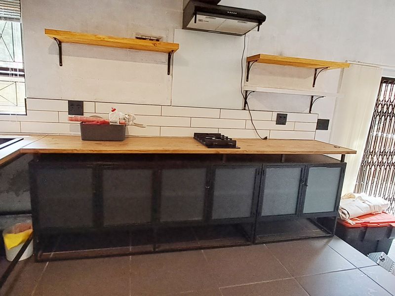 A rustic-style kitchen featuring a wooden countertop, gas hob, extractor fan, subway tile backsplash, and industrial-style metal cabinetry.