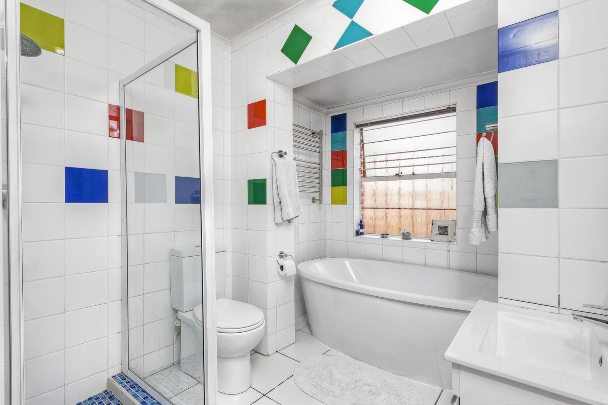 A functional bathroom featuring a glass-enclosed shower, a freestanding bathtub, a vanity basin, and a heated towel rail with decorative tiled accents.