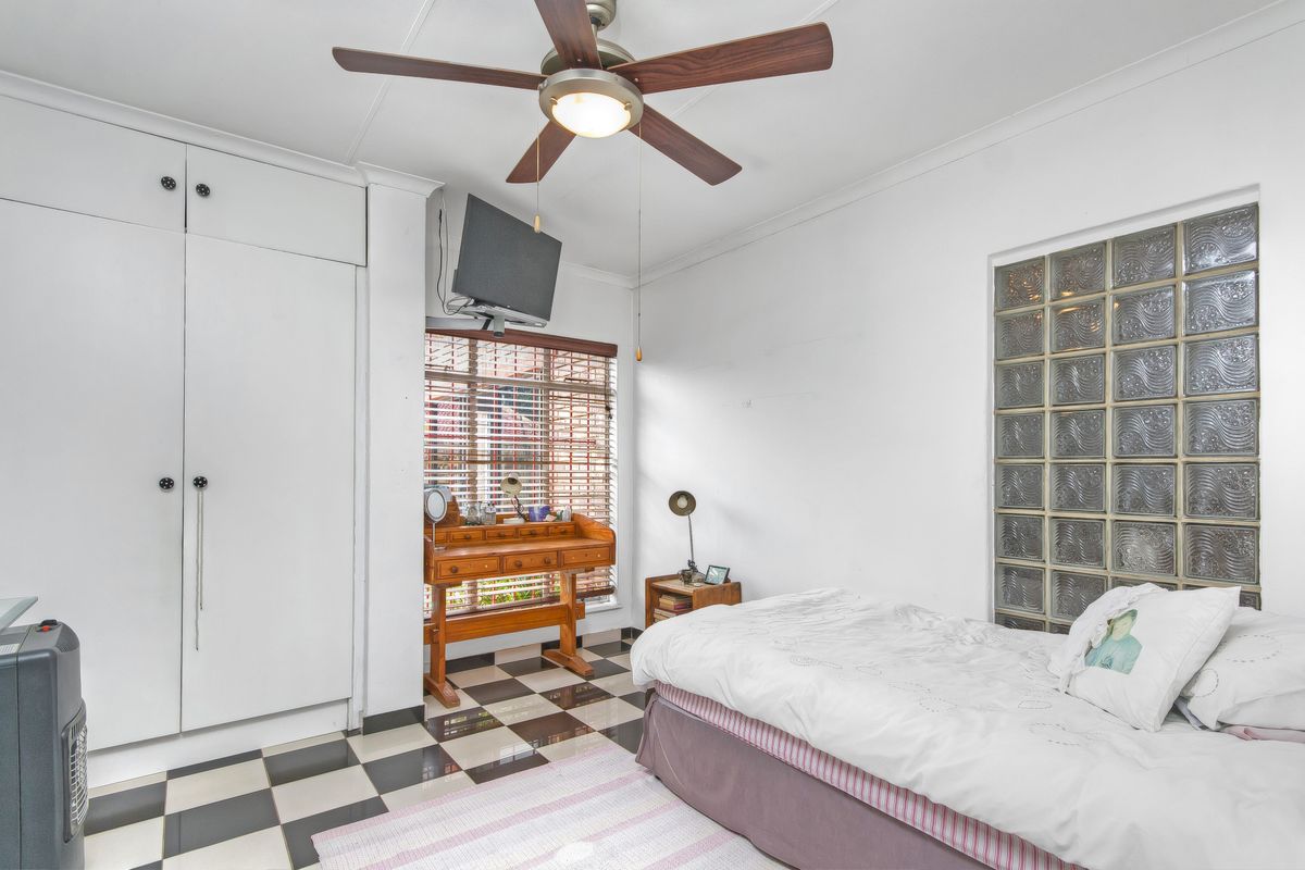 A bedroom featuring built-in cupboards, a ceiling fan, and a unique glass block feature wall with checkered tiled flooring.