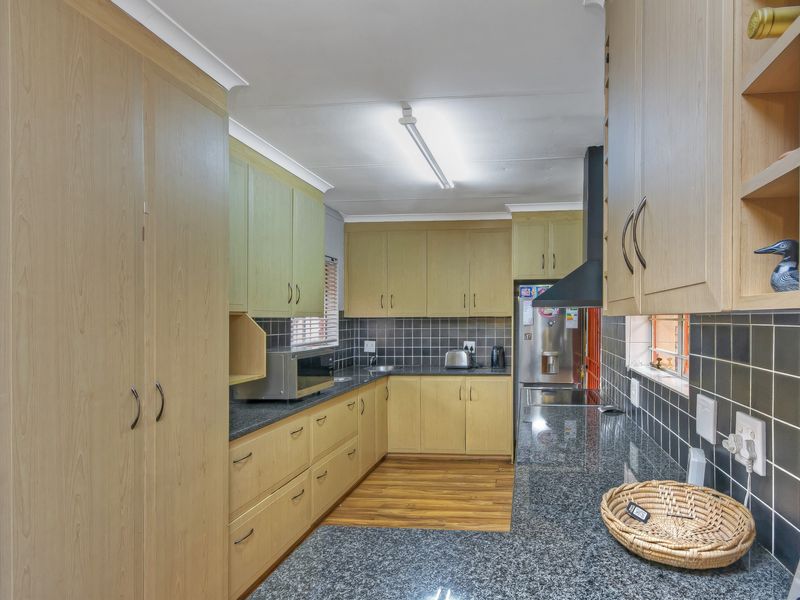 A functional kitchen featuring light wood cabinetry, dark granite countertops, a tiled backsplash, and integrated appliances, offering a practical workspace.