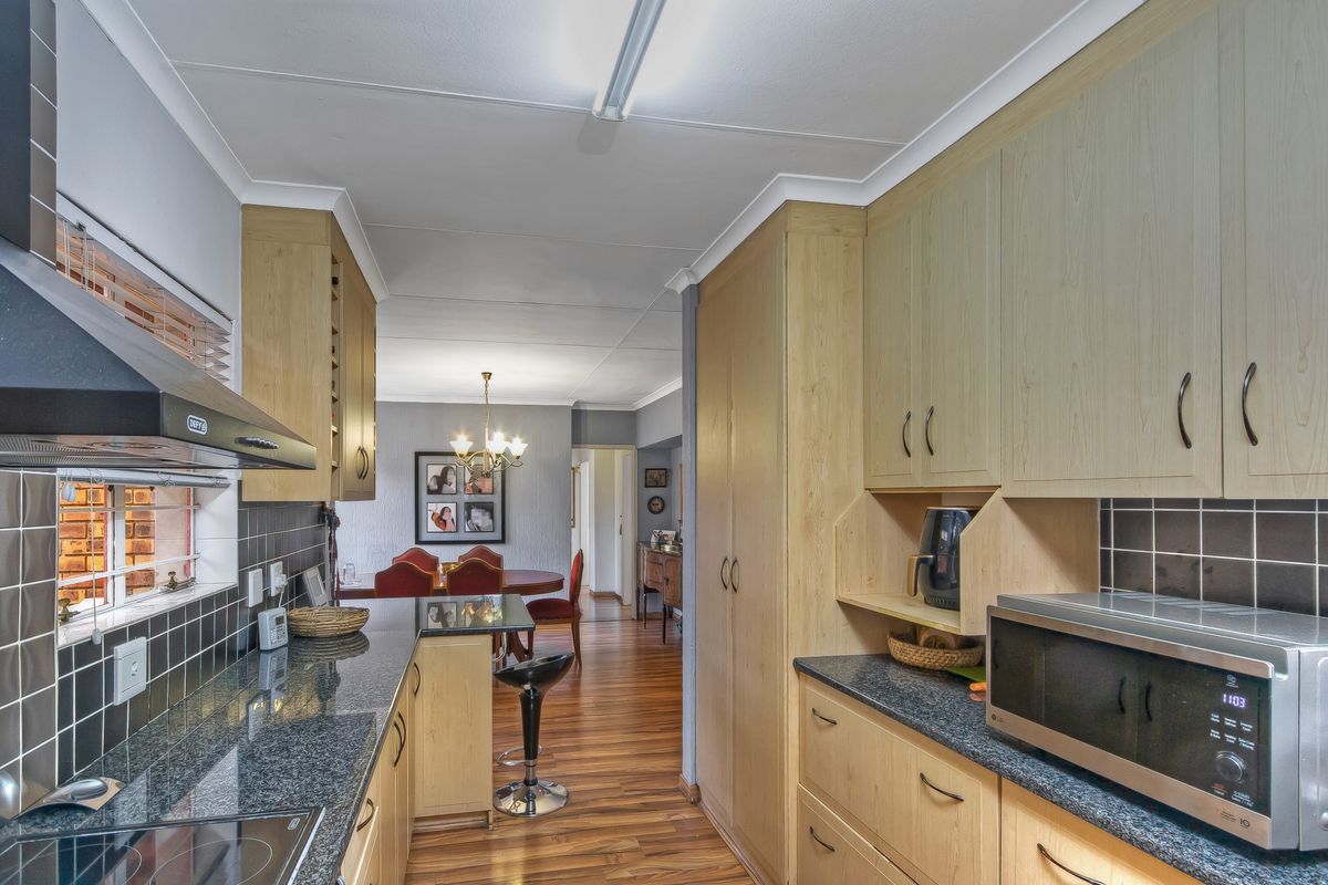 Functional kitchen featuring light wood cabinetry, dark granite countertops, tiled backsplash, and integrated extractor fan, flowing into the adjacent dining area.