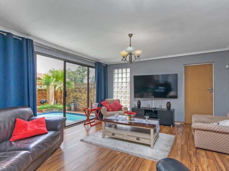Spacious living room featuring laminate flooring, a glass block feature window, and large sliding doors providing direct access to the outdoor pool area.