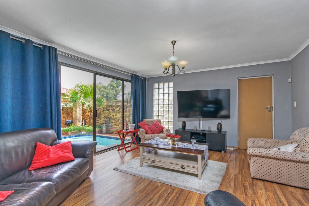 Spacious living room featuring laminate flooring, a glass block feature window, and large sliding doors providing direct access to the outdoor pool area.