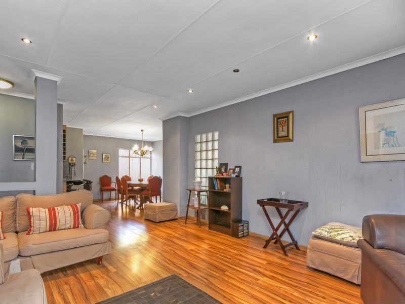 Spacious open-plan living and dining area featuring warm laminate flooring, recessed lighting, and a decorative glass block wall partition.