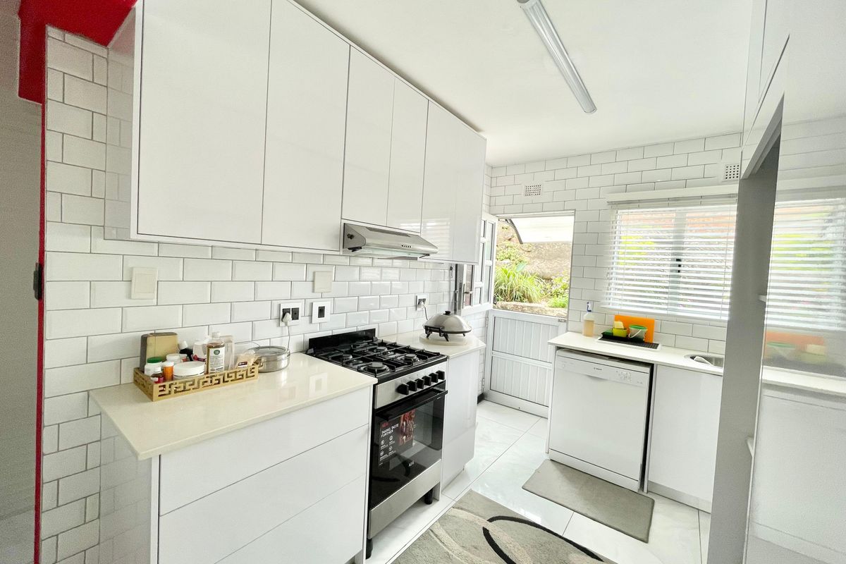 A modern, bright kitchen featuring white glossy cabinetry, subway tile backsplash, gas stove, and integrated dishwasher with direct access to the rear exterior.