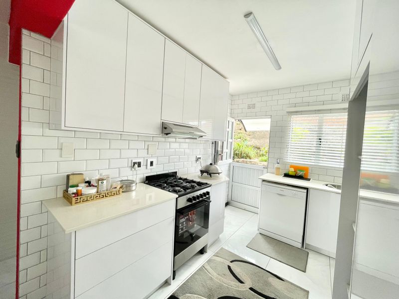A modern, bright kitchen featuring white glossy cabinetry, subway tile backsplash, gas stove, and integrated dishwasher with direct access to the rear exterior.