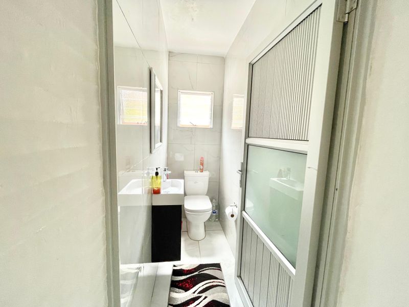 A compact bathroom featuring tiled walls, a vanity basin, a toilet, and a frosted glass door.