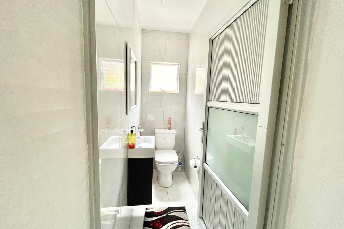 A compact bathroom featuring tiled walls, a vanity basin, a toilet, and a frosted glass door.