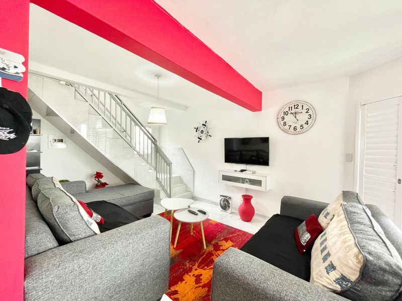 A bright living room featuring a staircase with a metal balustrade, tiled flooring, and a wall-mounted media console.