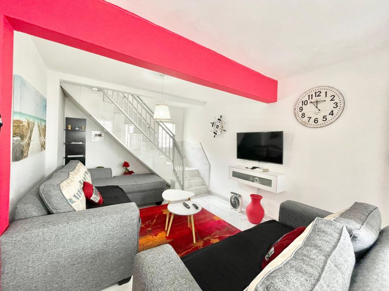 A living room featuring tiled flooring and an integrated staircase, providing a functional open-plan layout with a wall-mounted media console.