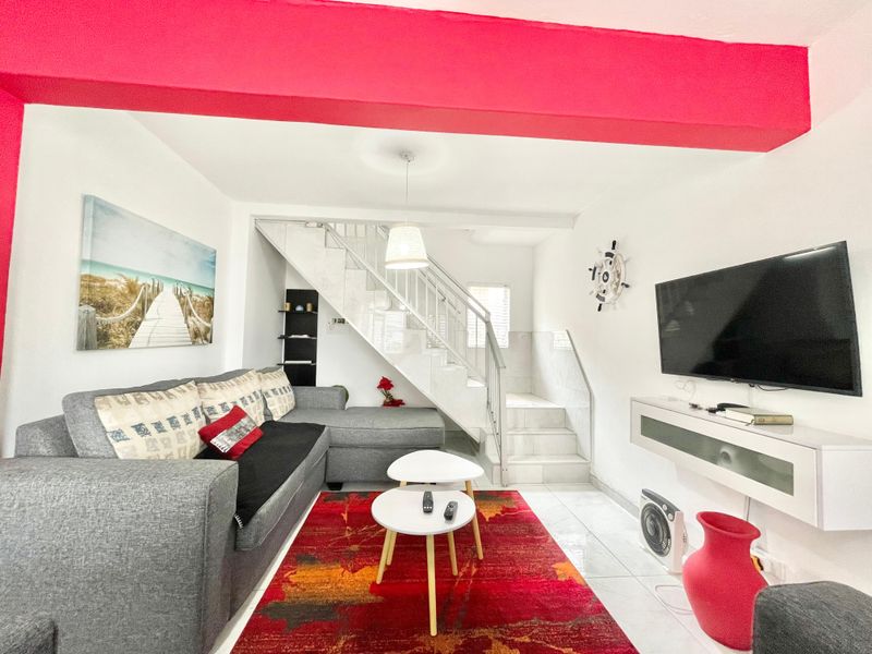 A living room featuring tiled flooring, a staircase with metal railings, and a wall-mounted media console.