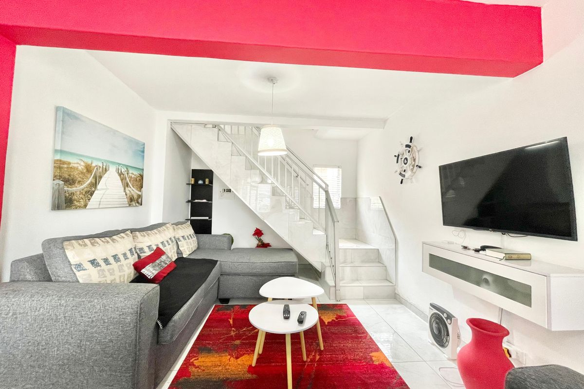 A living room featuring tiled flooring, a staircase with metal railings, and a wall-mounted media console.