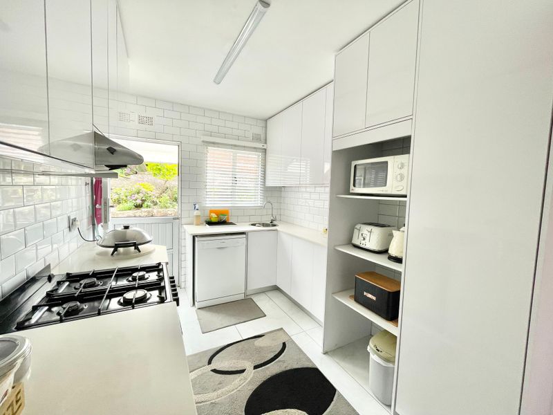 A bright, modern kitchen featuring white cabinetry, subway tile backsplash, gas hob, extractor fan, and direct access to the rear garden area.