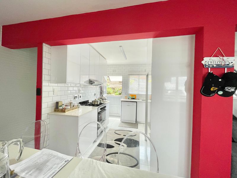 A bright, modern kitchen featuring white gloss cabinetry, subway tile backsplash, and integrated appliances, framed by a bold red structural archway.
