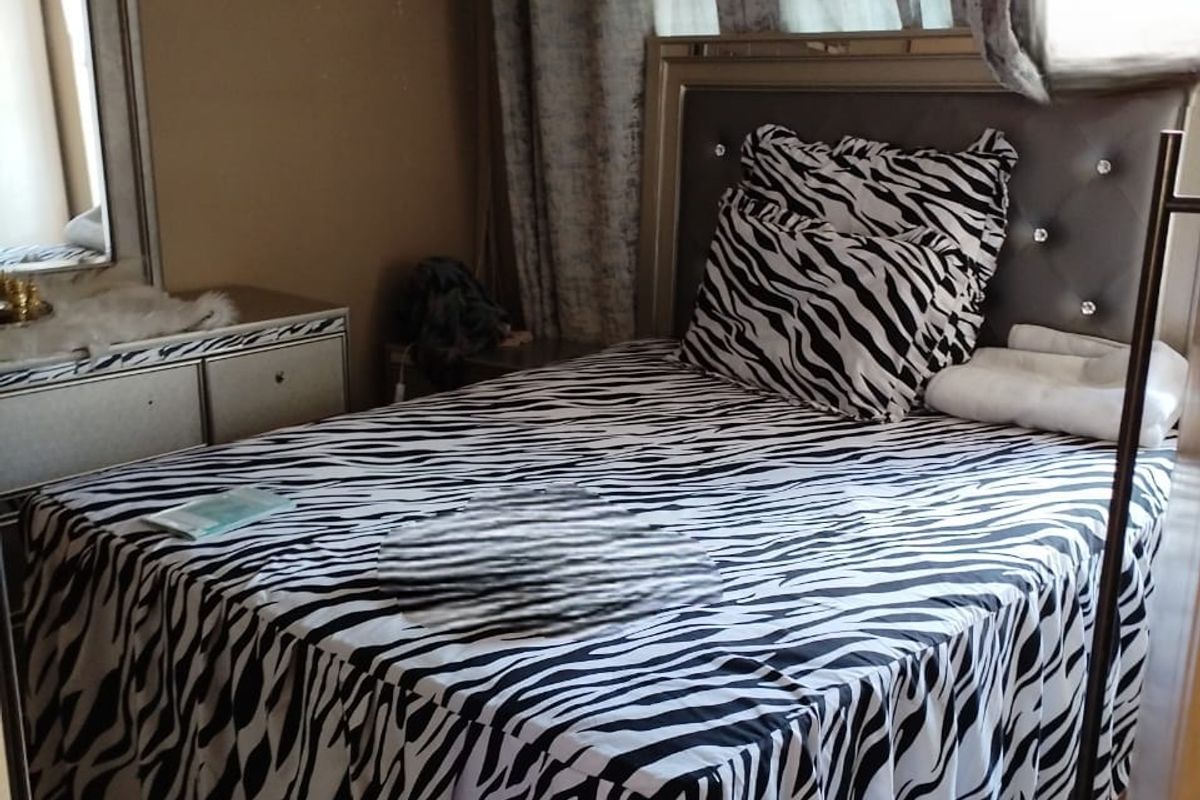 A bedroom featuring laminate flooring, a built-in headboard, and window treatments.