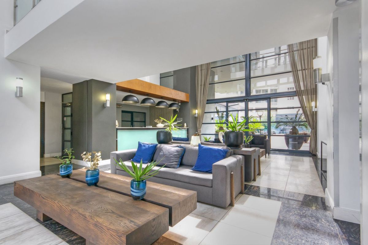 Spacious modern lobby or communal living area featuring double-volume ceilings, large glass windows, tiled flooring, and a built-in reception desk.