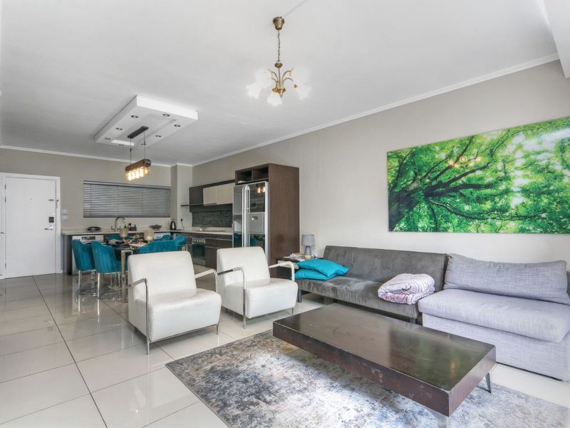 Open-plan living and dining area featuring tiled flooring, modern kitchen cabinetry, and integrated lighting fixtures in a well-maintained apartment setting.