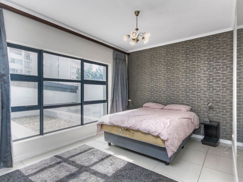 A bedroom featuring large aluminum-framed windows, tiled flooring, and a decorative feature wall with patterned wallpaper.