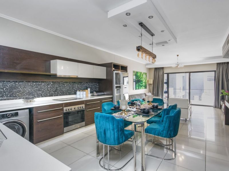 Modern open-plan kitchen and dining area featuring sleek cabinetry, integrated appliances, tiled flooring, and direct access to a balcony.