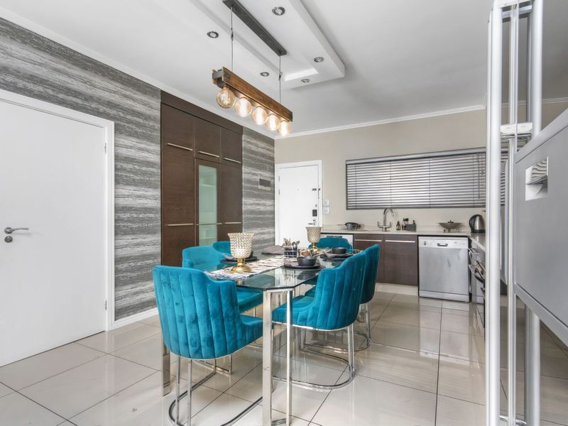 Modern open-plan kitchen and dining area featuring sleek cabinetry, tiled flooring, recessed ceiling lighting, and a contemporary pendant light fixture.