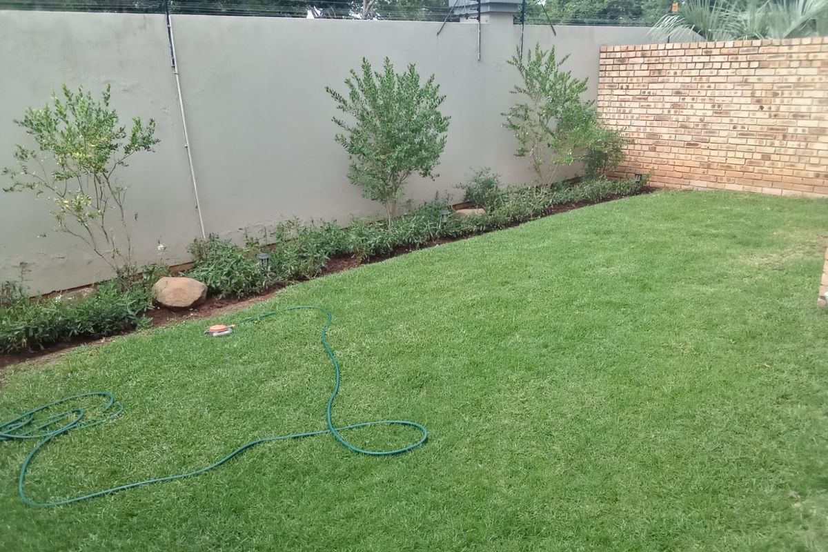 A private rear garden featuring a well-maintained lawn, landscaped garden beds, and secure perimeter boundary walls with electric fencing.